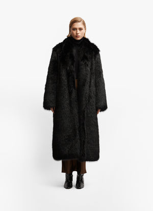 Model facing forward wearing luxe black faux fur maxi coat against white brackground.