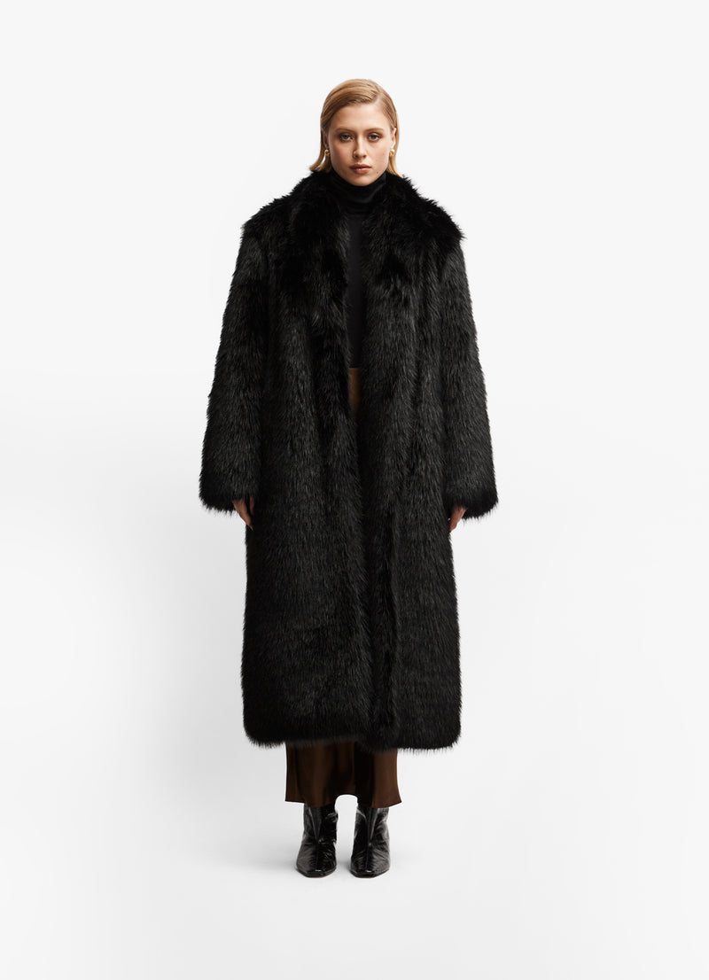Model facing forward wearing luxe black faux fur maxi coat against white brackground.