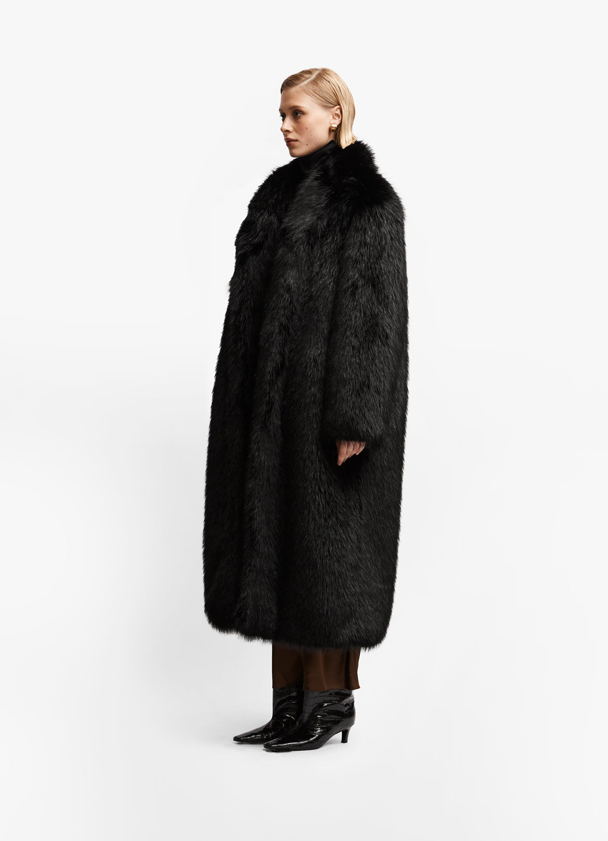 Side profile of model wearing luxe black faux fur coat against white backdrop.