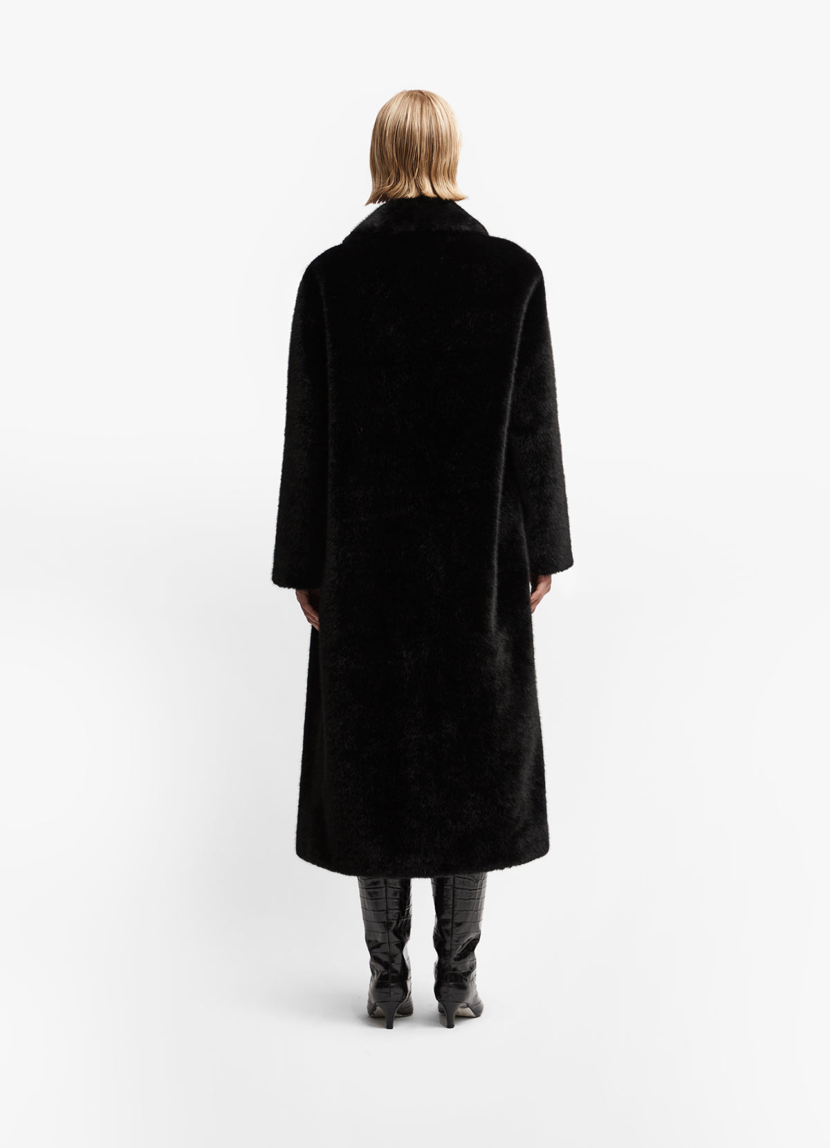 Back view of model wearing black faux fur long coat against white backdrop.