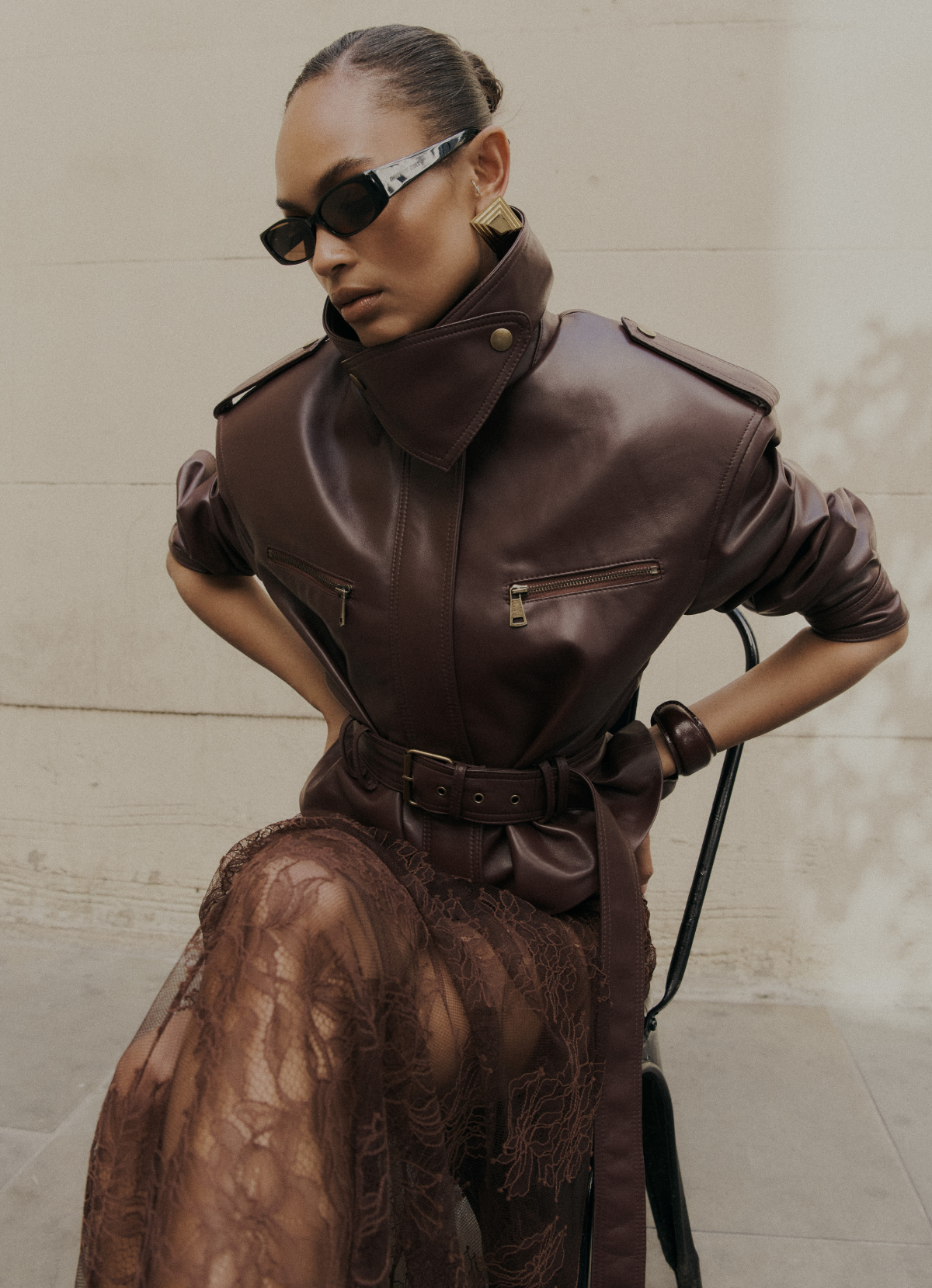 Model wearing burgundy cropped leather jacket with hands on waist, showing collar up and jacket details.