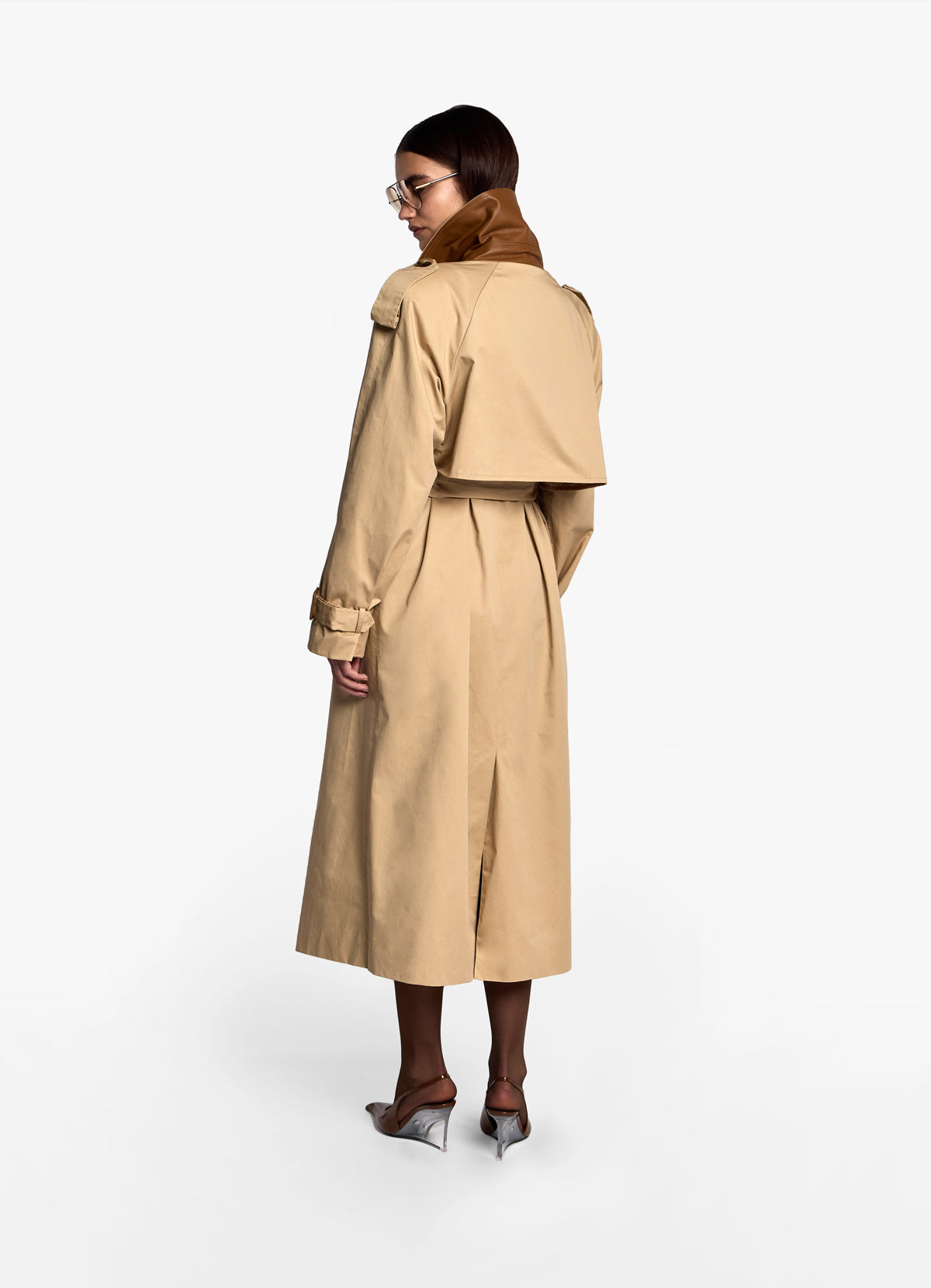 Back view of model in cotton trench coat with collar up revealing leather trim underneath. 