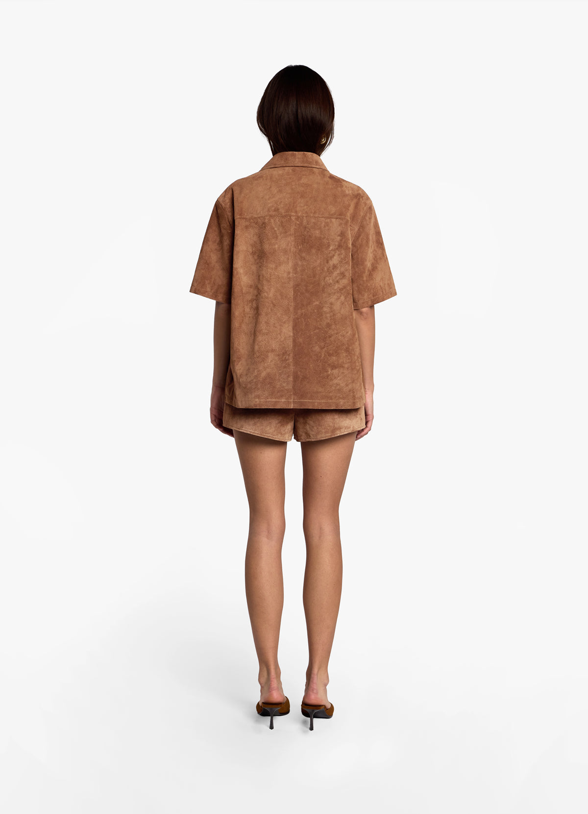 Back view of model wearing mocha suede shirt, hair tucked in to show collar, paired with matching mocha suede shorts. 