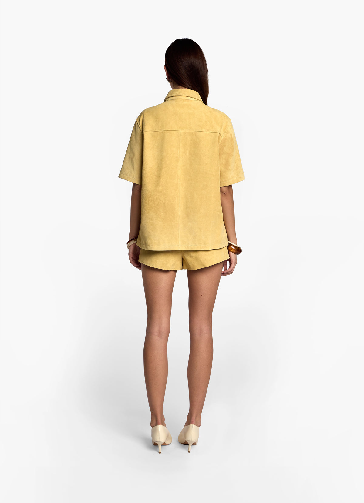 Back view of model wearing butter yellow suede shirt with matching suede shorts.