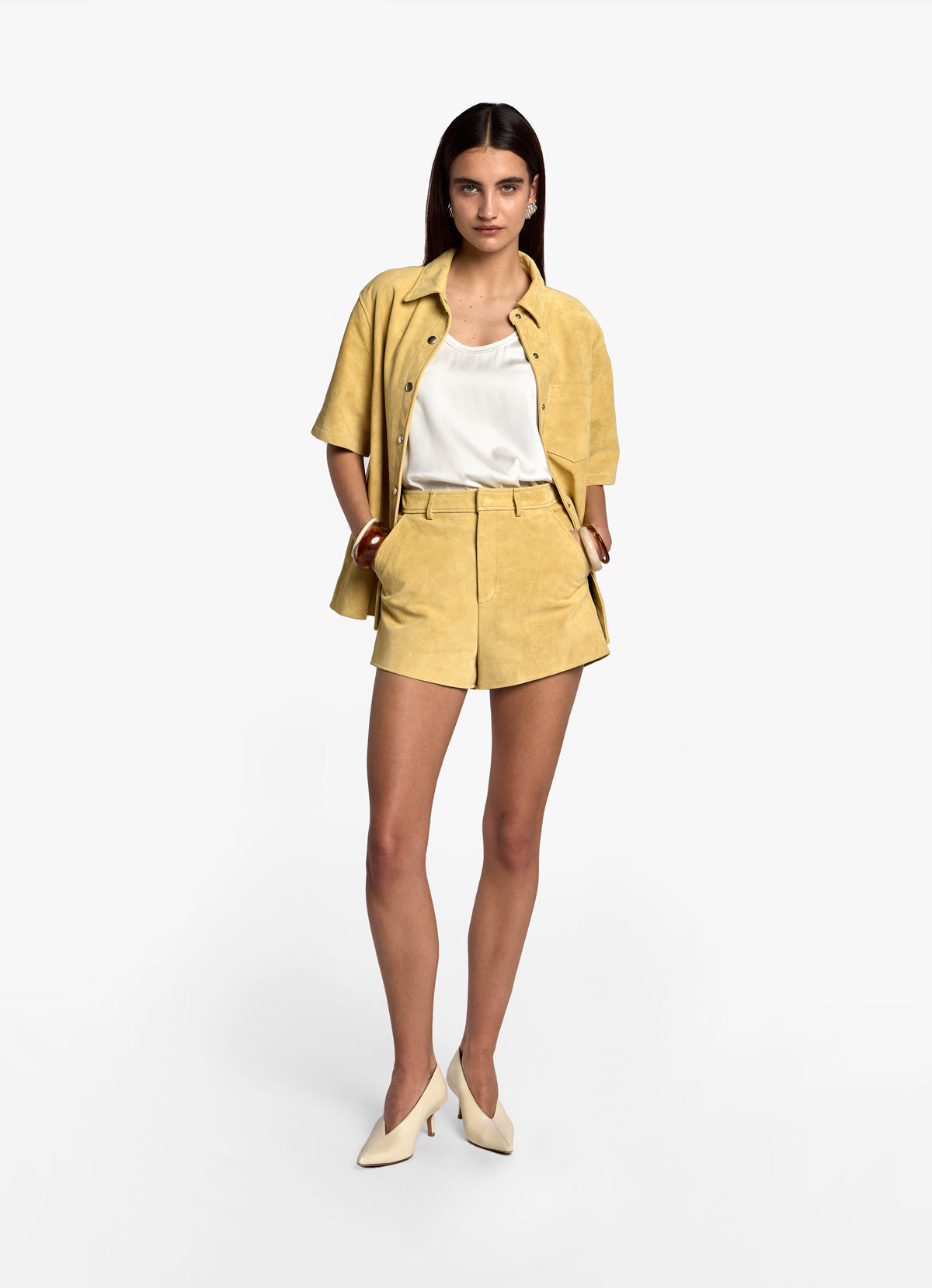 Model wearing butter yellow suede shorts, facing forward with hands in pockets.