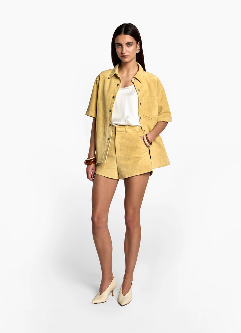 Front view of model wearing butter yellow suede shorts, showing short length and pocket detail.