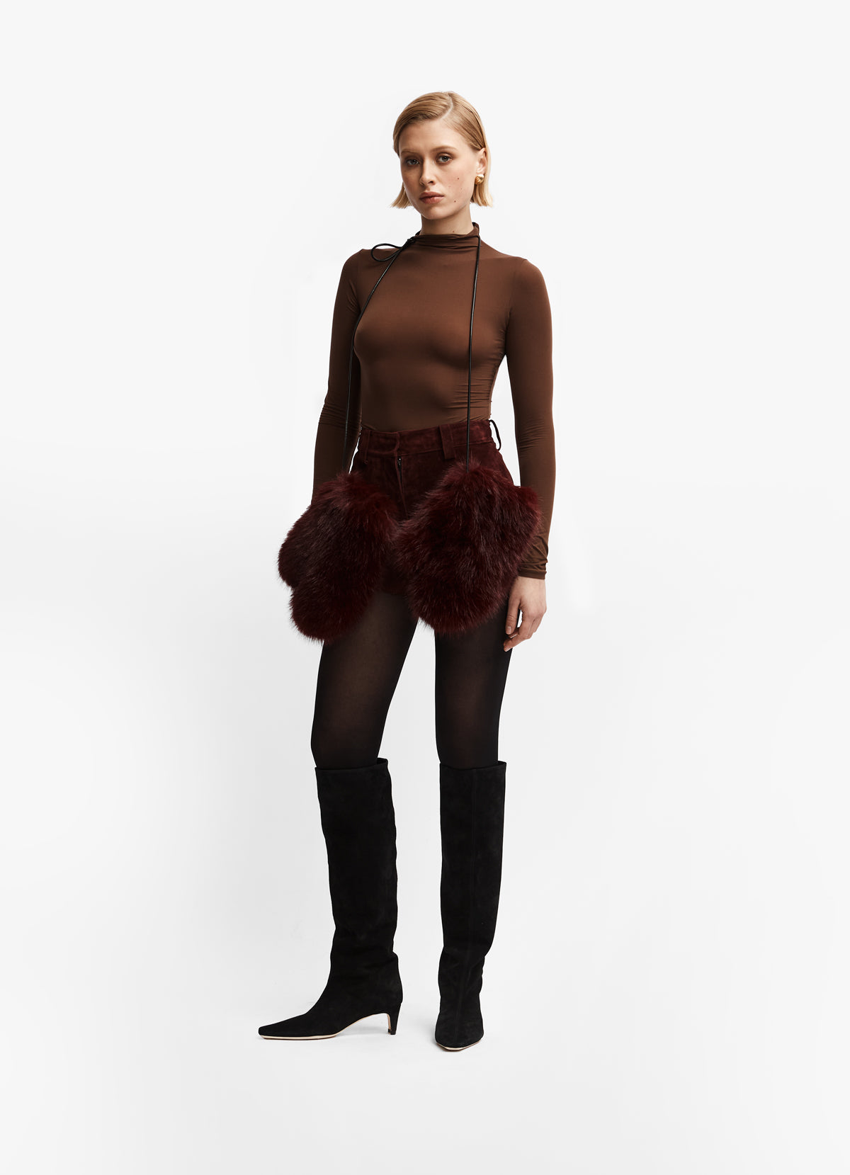 Model wearing burgundy faux fur mittens with leather strap around neck against white background.