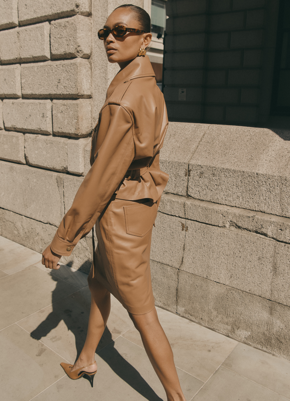 Model walking away wearing mocha leather jacket and matching leather pencil skirt.