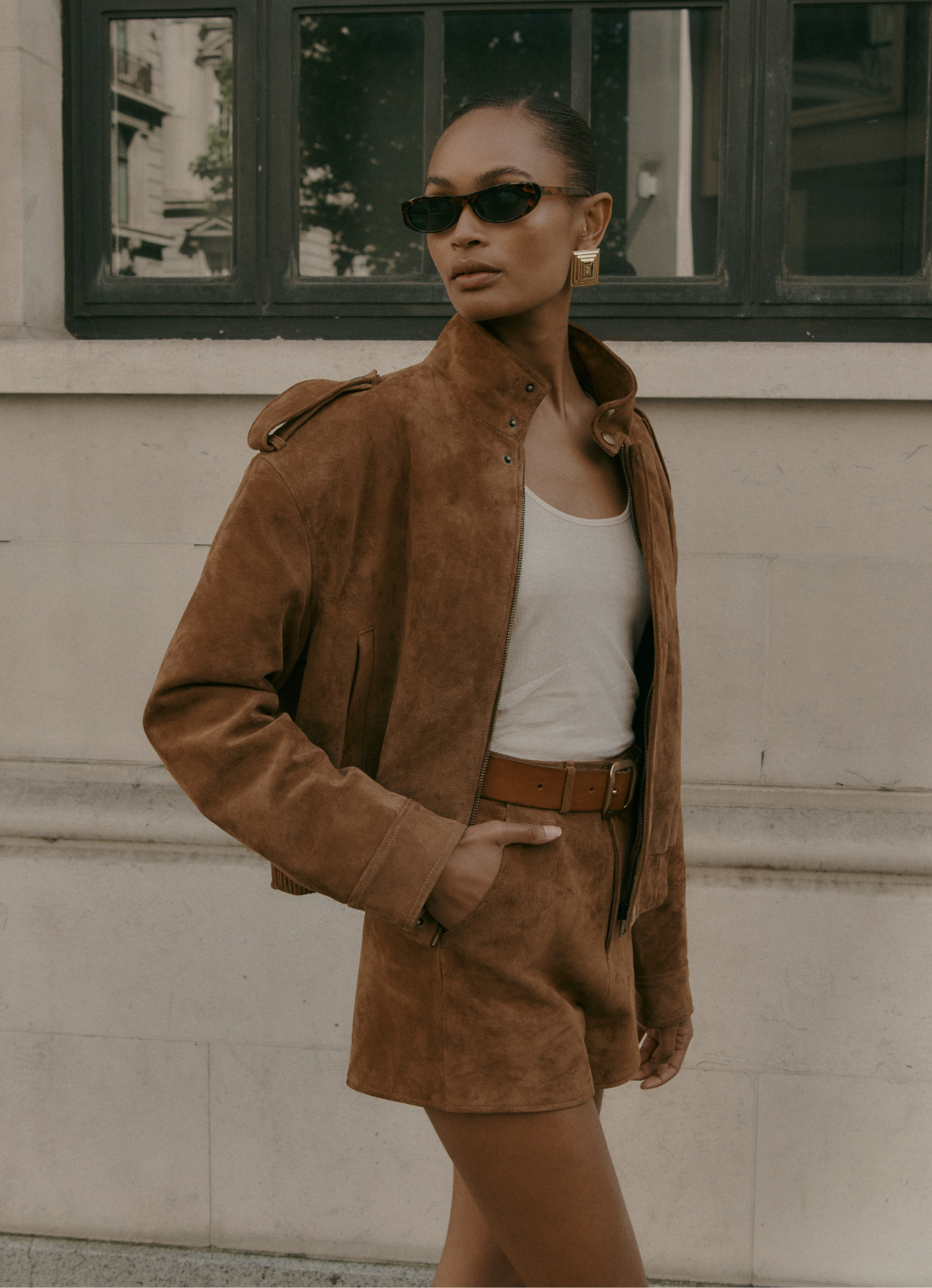 Torso shot of model looking away and walking wearing the de Savary London mocha suede bomber jacket with matching shorts.