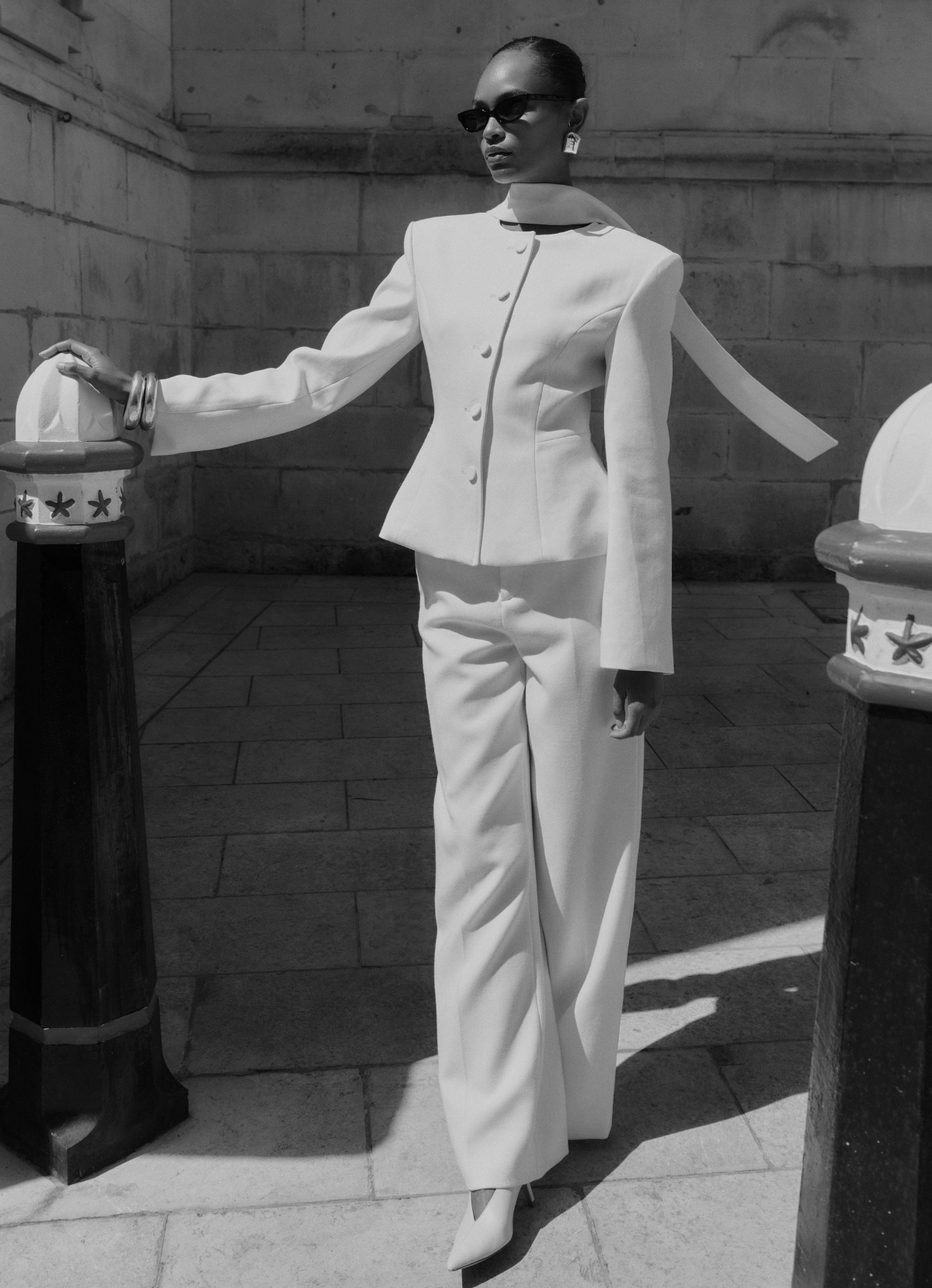 Black and white image of model looking away wearing white fitted suit with neck scarf.